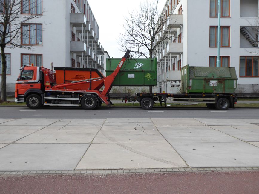 Orange garbage truck with green containers in urban Amsterdam, showcasing industrial city life.